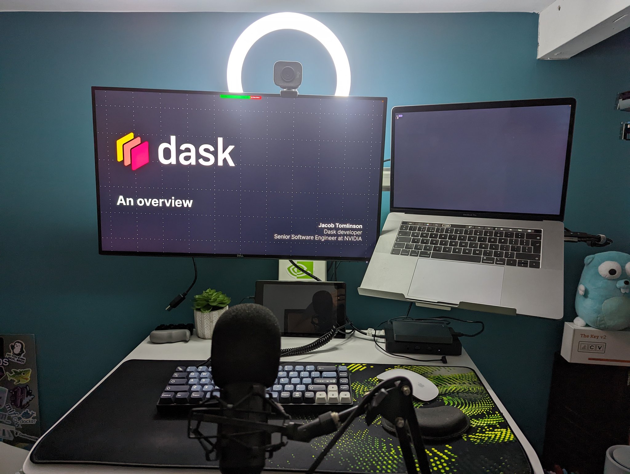 Photo of my desk with my camera, microphone and lighting set up for a talk with my Dask slides on the screen